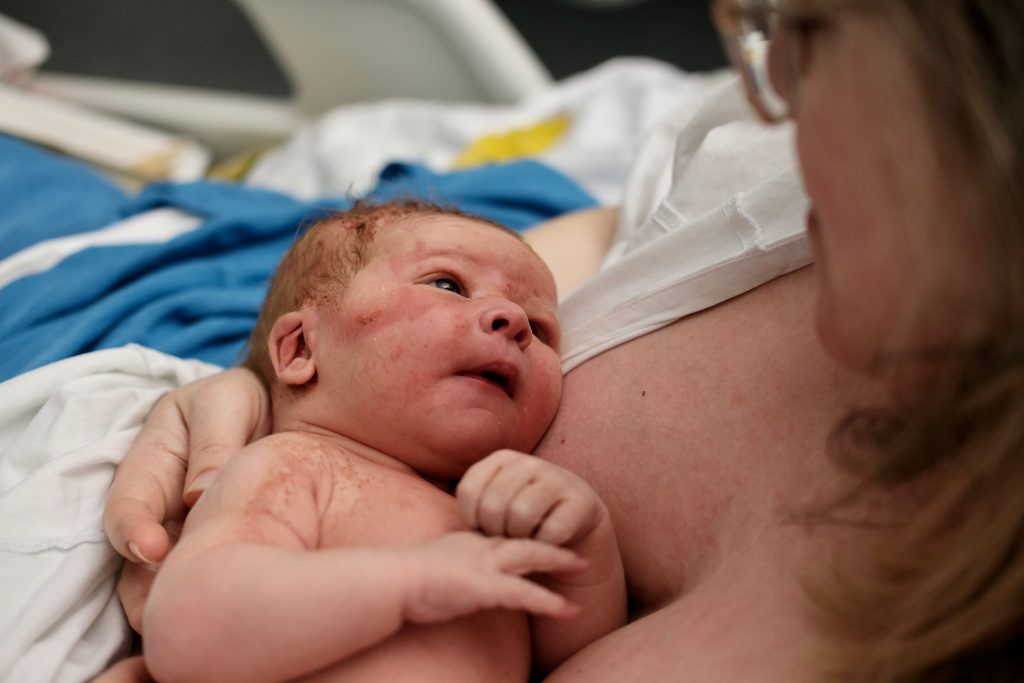 A newborn baby, Elias, in his mother Andrea's arms looking up at her obscured face