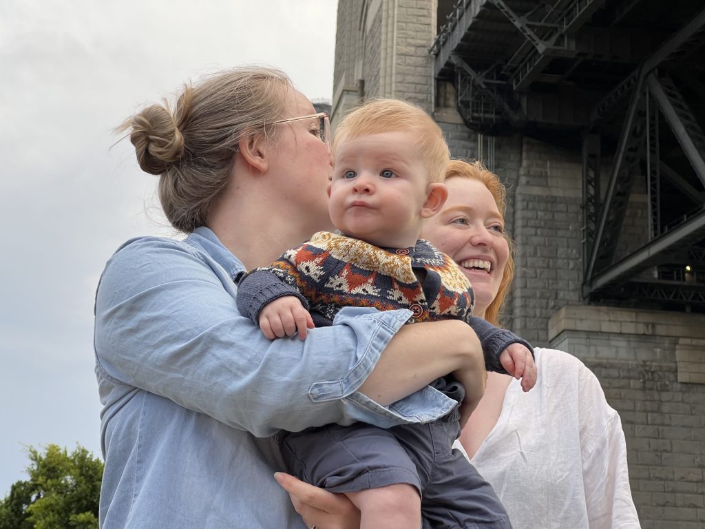 Andrea holds Elias and stands next to her sister Elise under the Sydney Harbour Bridge.