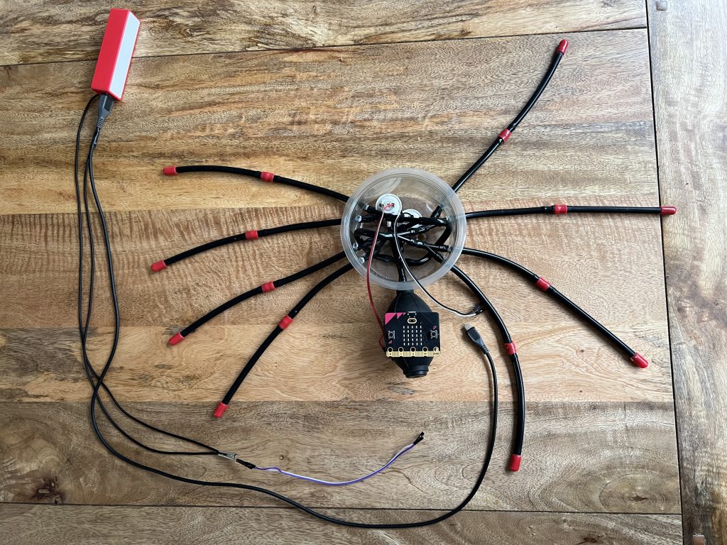 The skeleton of a toy spider, showing the rubber tube legs and the connections to a single thread web of variable conductivity rubber. The legs are joined inside a circular clear plastic container.