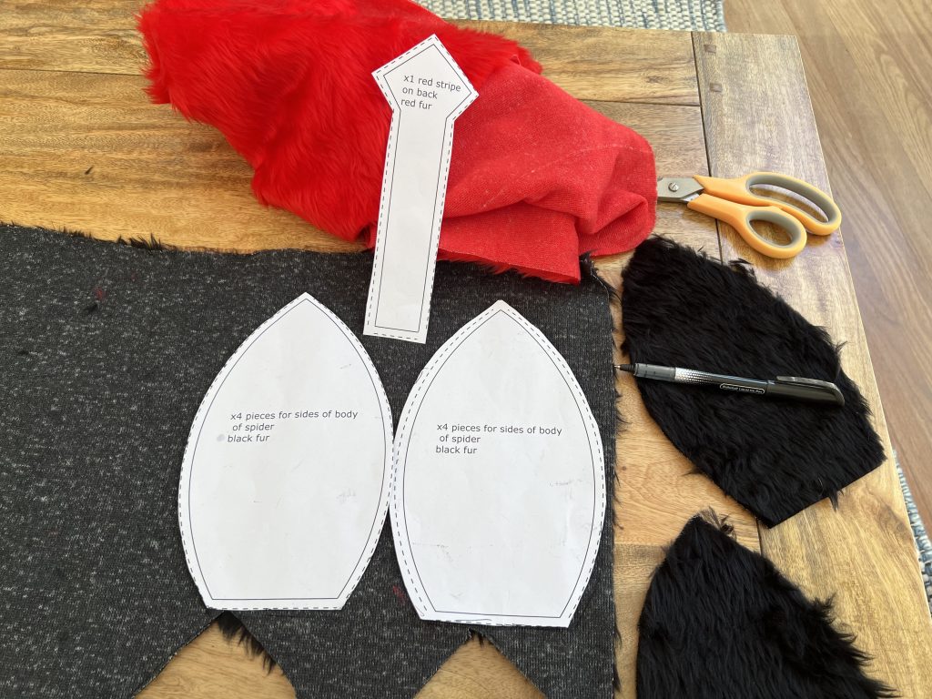 Some black and red material lie on a table with scissors and three paper patterns for cutting shapes.