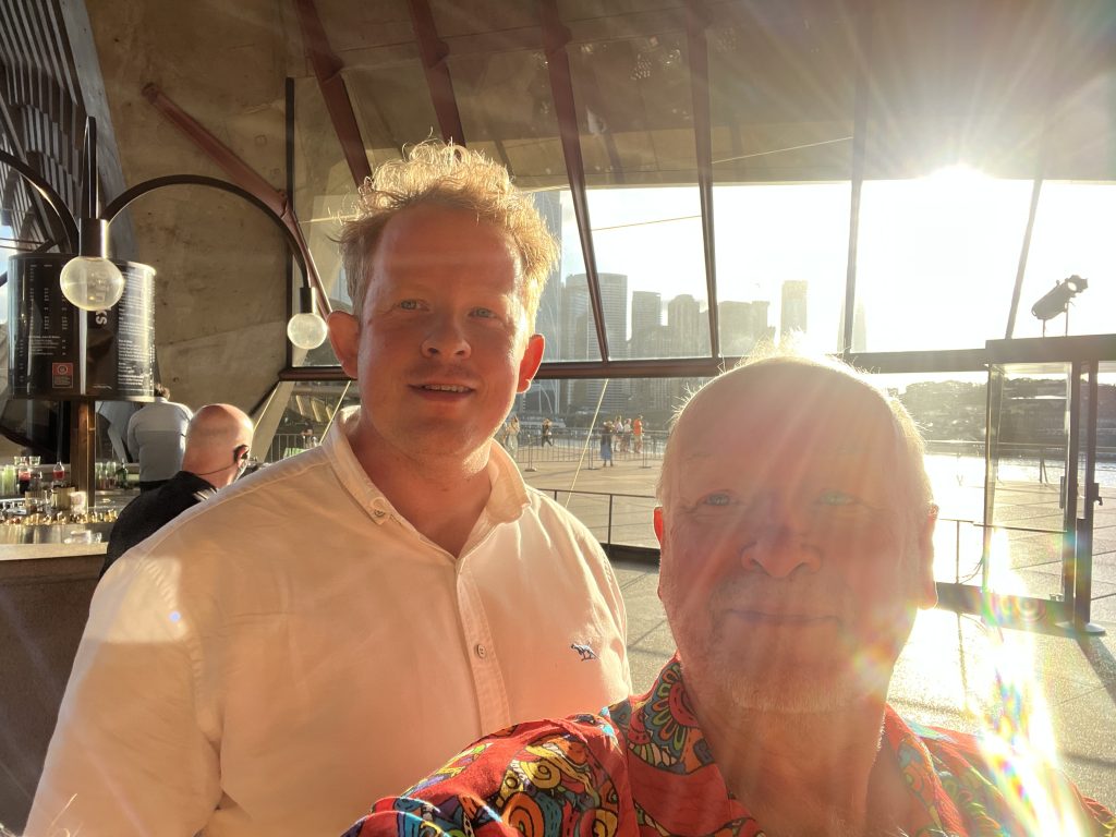 Patrick and me standing inside the Opera House with the setting sun and Sydney Central Business District through the window.