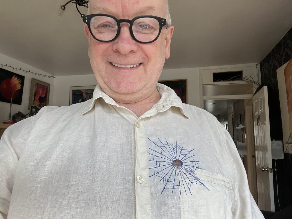 A man with a holey shirt repaired using a Sashiko technique of embroidery designed to look like a spider's web.