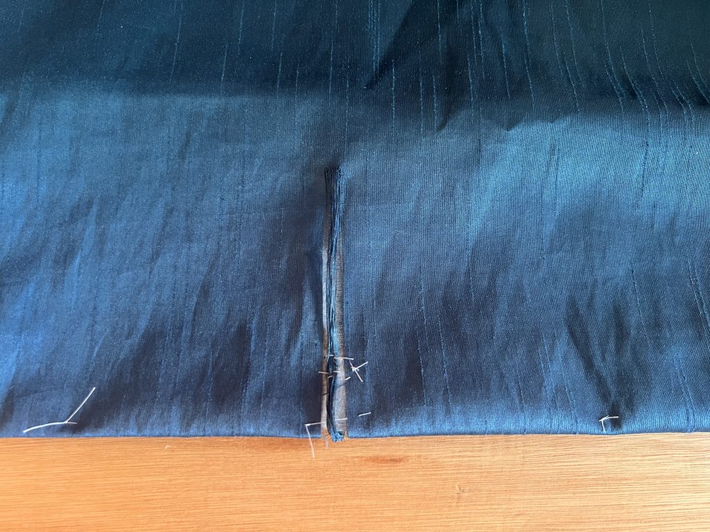 Torn curtain material with a few hand stitches to hold it together in preparation for repair.