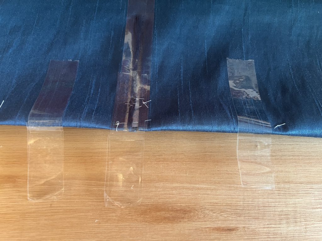 Torn curtain material with a few hand stitches and sellotape to hold it together in preparation for repair.