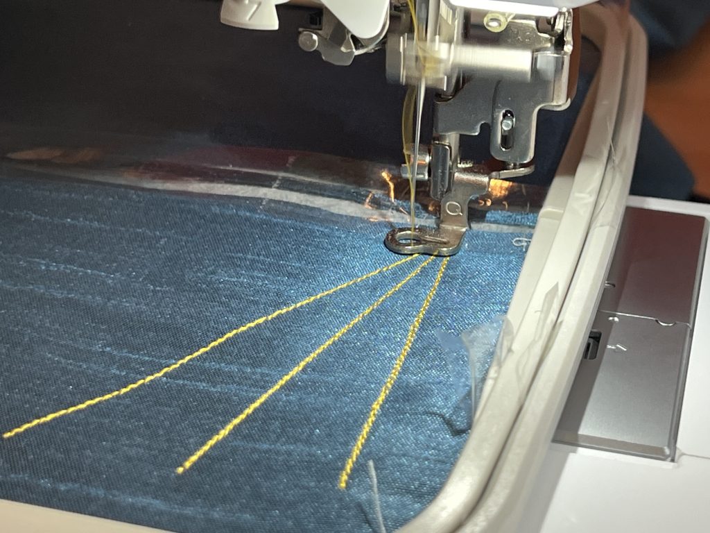Material in an embroidery machine frame being stitched with three lines of thread.