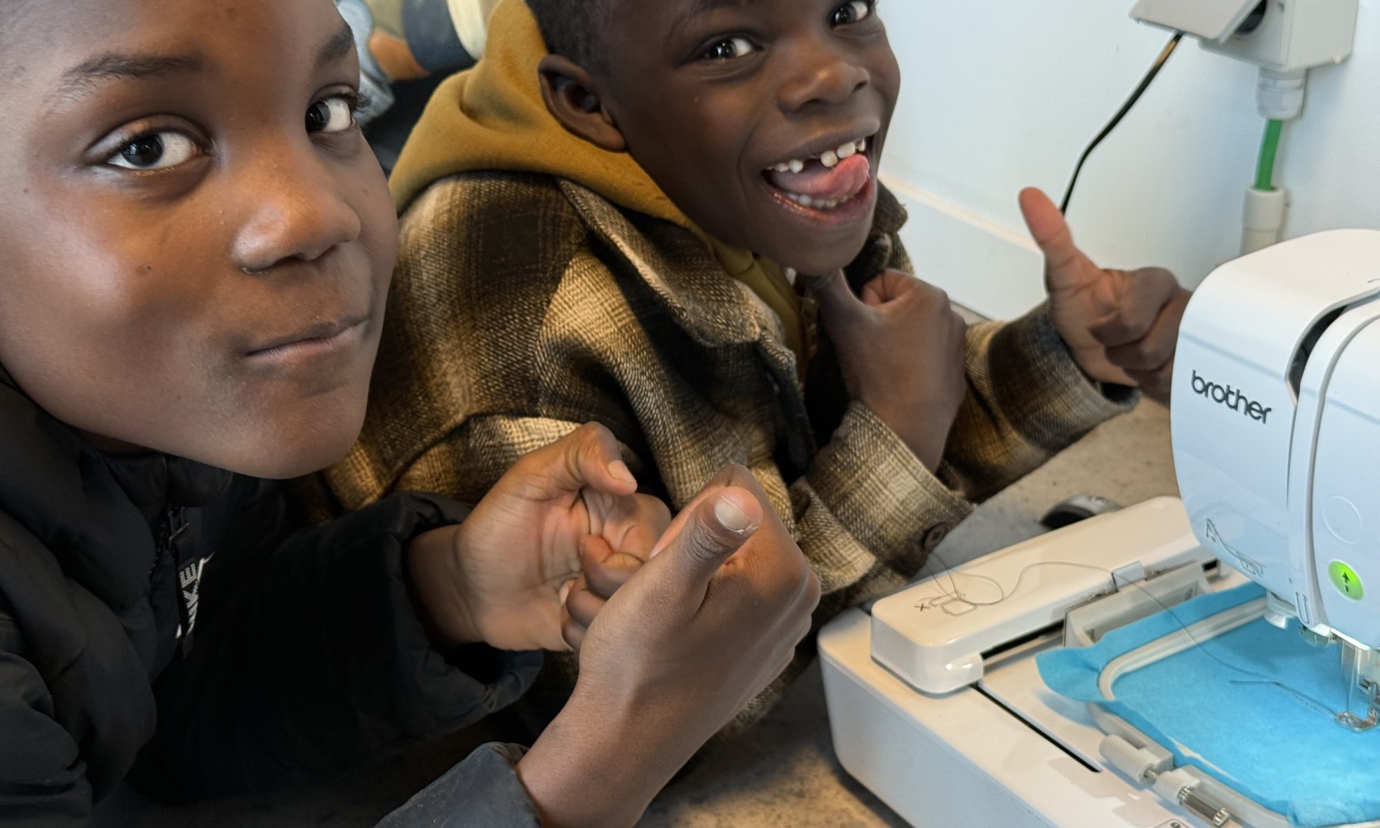 Two boys watching their embroidery being stitched on the machine